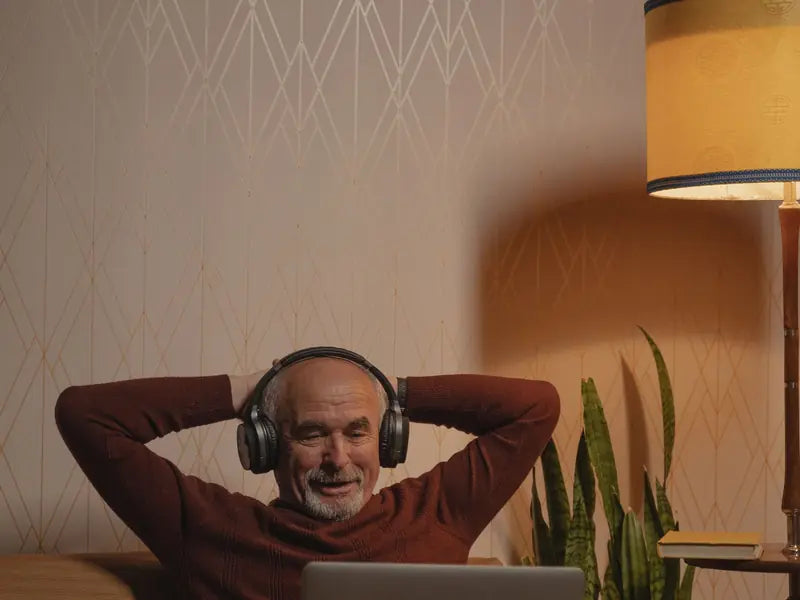 A man relaxing with headphones in front of his laptop at home