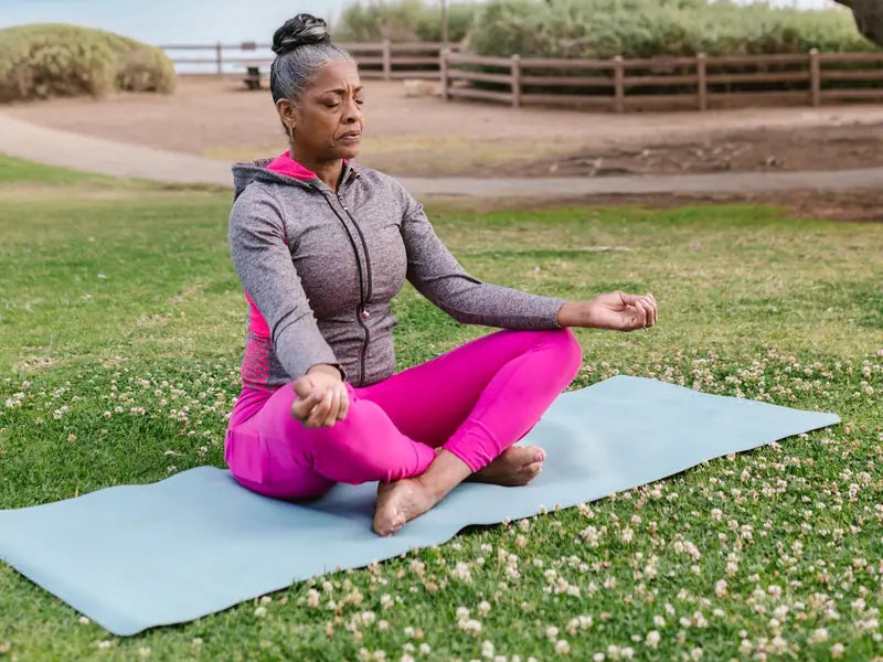 A woman meditating on a mat outdoors in a park